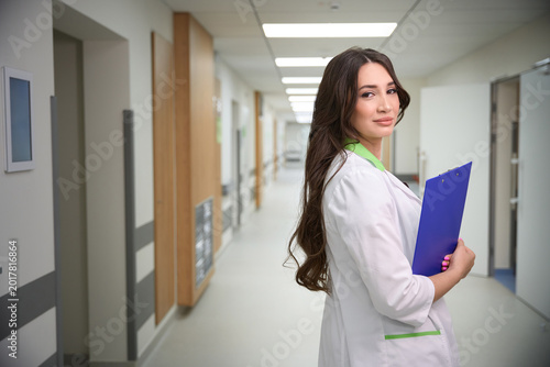 Caucasian woman doctor in white lab coat with clipboard in hospital