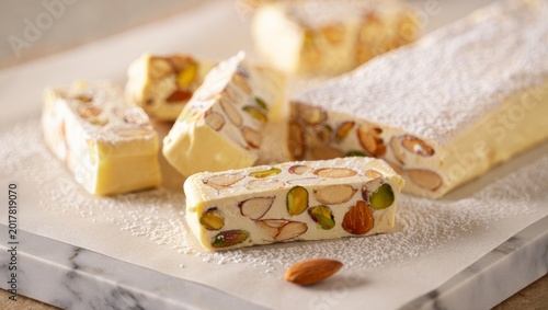 Almond and pistachio nougat pieces with powdered sugar, a sweet dessert confection on white marble