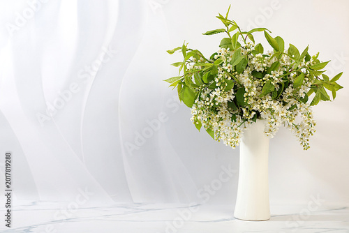 Abstract floral arrangement and banner for the screen. A still life with beautiful spring branches of blooming bird cherry in a vase against an elegant background. A floral holiday card