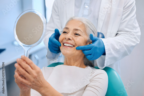 Smiling Elderly Woman at Dental Appointment Holding Mirror in Modern Clinic