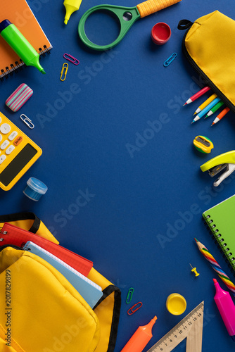 Back to school vertical supplies flat lay with yellow backpack and colorful stationery on blue background