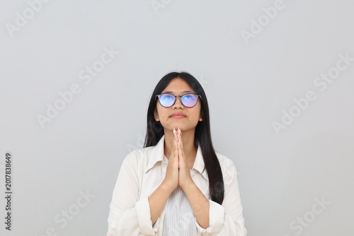 Canvastavla A young Asian woman is praying, looking up and pleading with a hopeful expression, asking for forgiveness, putting her hands together in front of her chest, isolated on a white background