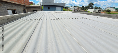 Photos Modern rooftop with gray corrugated fiber cement and standing seam metal roofing, masonry parapet walls, bright daylight, and contemporary residential neighborhood background