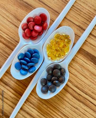 Top view of colorful capsules, fish oil supplements, and vitamins displayed in ceramic spoons on a wooden table. Healthy lifestyle, dietary supplement, nutrition, wellness