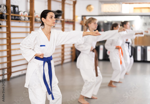 Vászonkép Assertive young woman practicing punches standing in row with others during kara