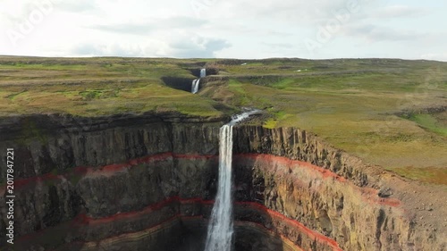 Aerial flight over the famous Hengifoss waterfall on a summer day in east Iceland. It has basaltic strata with thin, red layers of clay between the basaltic layers.