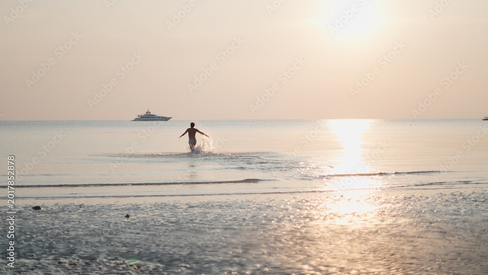 Fototapeta premium Man running in ocean at golden hour, celebrating freedom and luxury travel lifestyle