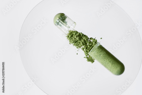 Open capsule spilling green powder on white surface, representing natural health