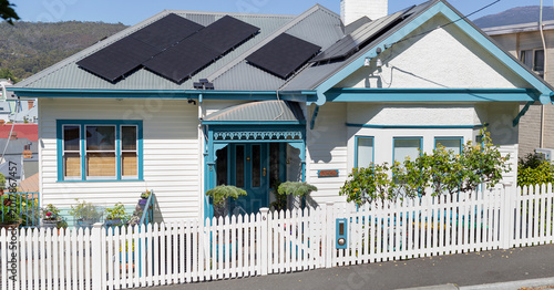 White weatherboard house with a white picket fence and solar panels on the roof