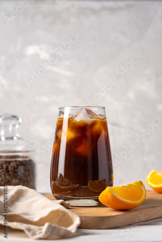 Coffee with orange juice bumble in a tall glass with ice on a light background with coffee beans, fruits and morning shadows