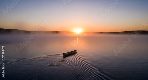Small boat on calm misty lake at sunrise