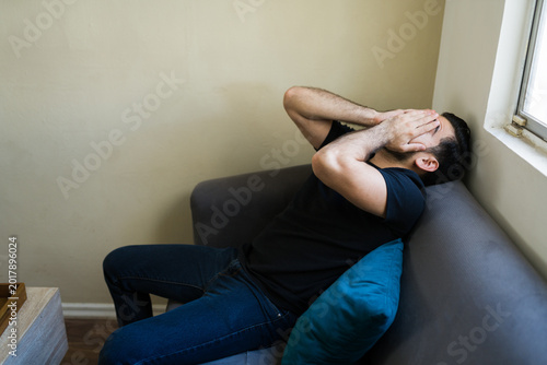 Foto Stressed man sitting on sofa and covering face feeling overwhelmed by mental hea