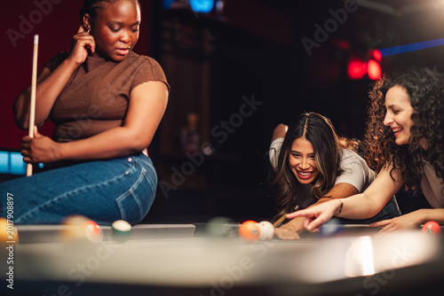 Obraz na plátně Diverse young women friends enjoying billiards in a lively pub, having fun playi