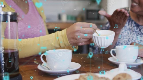 Daughter spooning sugar into cup offering mom care in kitchen, tech icons drifting over hands, cups