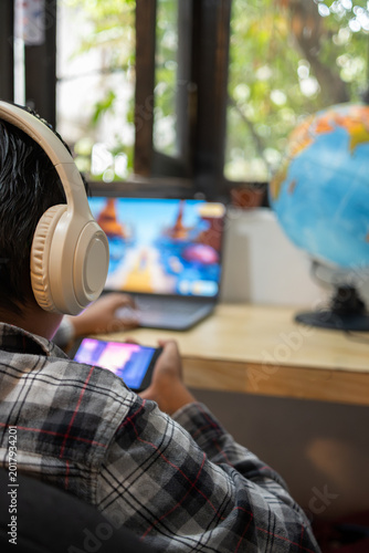 Teenager using headphones and playing video games on laptop and smartphone