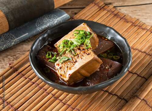 Schilderij op canvas A bowl of tofu and eggplant in a savory sauce on a bamboo mat with a mortar