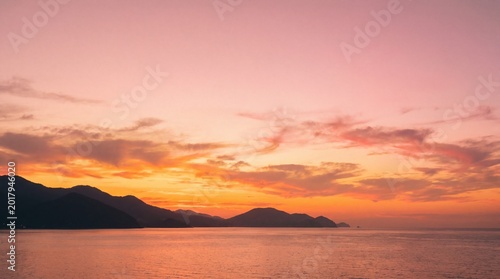 Warm sunset over calm sea with mountain range at horizon serene landscape