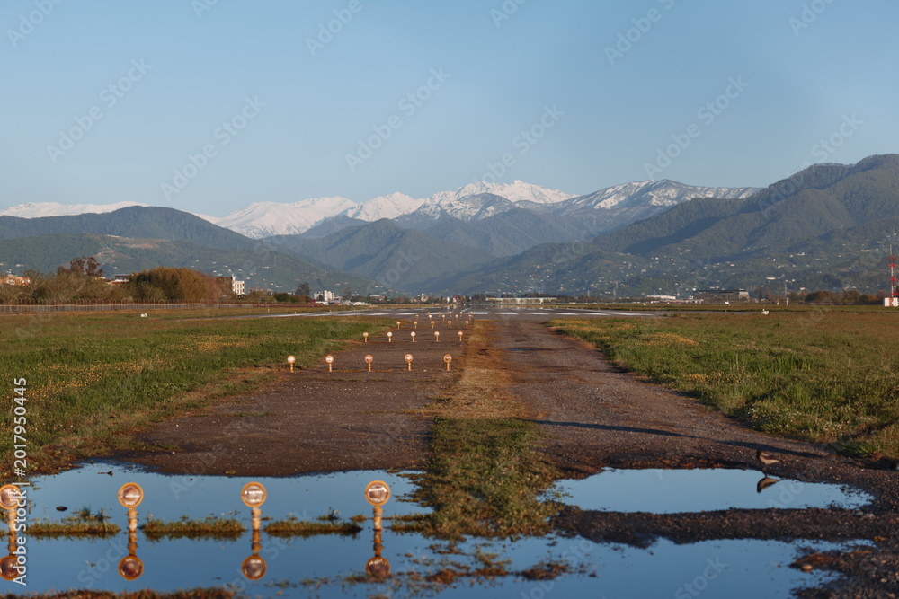 Obraz premium A dirt road cuts through a vast field toward distant snowcapped mountains beneath a clear blue sky, creating a tranquil, expansive rural landscape with peaceful solitude