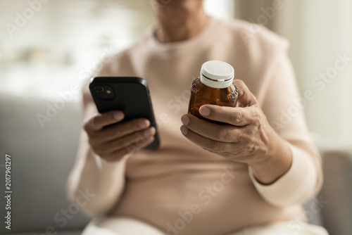 Konstfotografi Senior woman using hand for holding smartphone and medicine bottle while reading