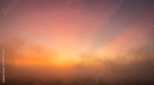 Blurred sunset glowing with warm orange and pink hues fading into a soft smoky atmosphere