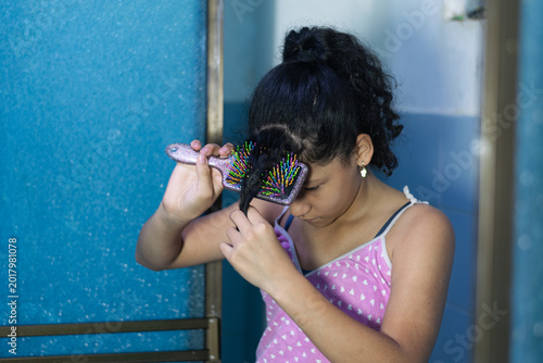 Latina girl combing curly hair in modest home while getting ready during morning routine