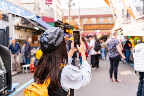 Young woman tourist with using her smartphone to capture images of local street food and crowds at Tsukiji Fish Market
