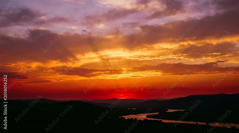 Fototapeta premium Vibrant golden hour sunset sky with deep orange and purple gradient over calm landscape