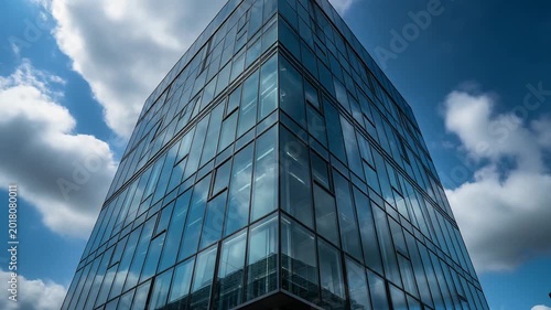 A sleek glass office building stands tall under a cloudy blue sky.