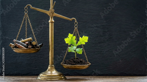 Balance scale weighing bullet casings versus green seedling on dark background, symbolizing peace, environment, and life's value.