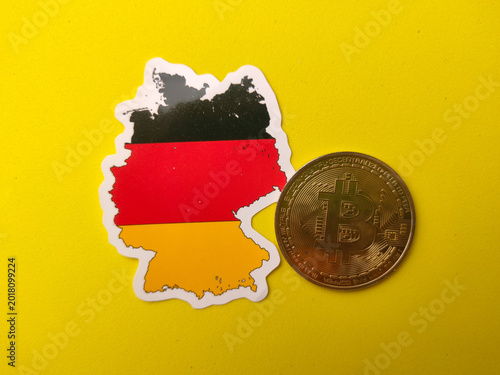 Germany flag-colored map sticker next to a gold Bitcoin physical coin on a bright yellow surface