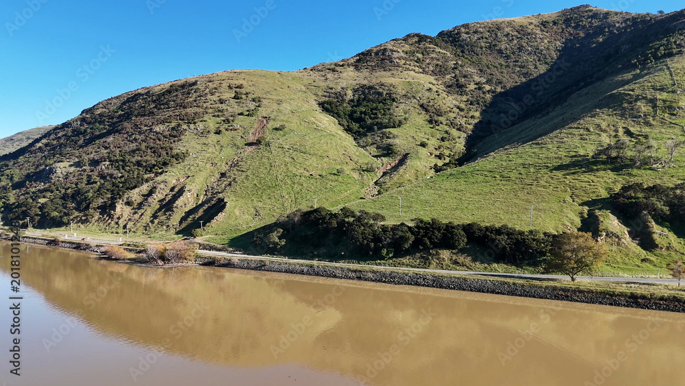 Obraz premium Aerial View of Green Hills and Murky Water in Akaroa New Zealand