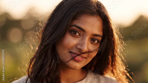 Close-up portrait of an attractive young Indian woman looking directly at the camera with a gentle, serene smile