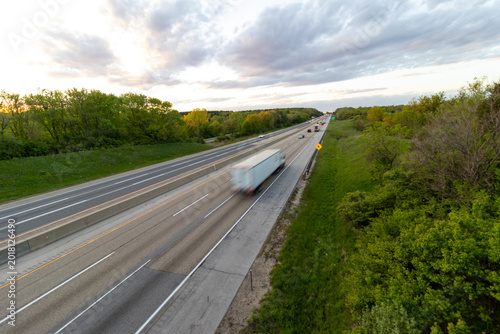 A slow shutter photo creating blur of a white semi truck with a white trailer driving down the highway road. 
