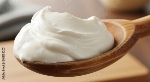 Creamy white sour cream or yogurt on a wooden spoon, smooth dairy product close-up shot.