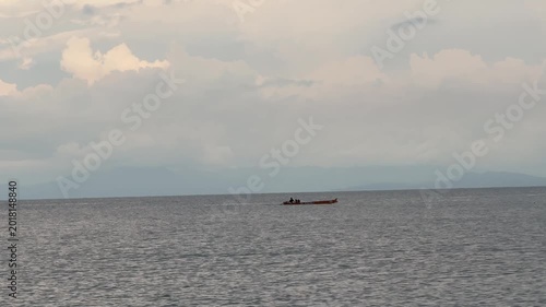 Distant Traditional Fishing Boat Traversing Calm Ocean Waters Under a Cloudy Sky with Hazy Mountains in the Background