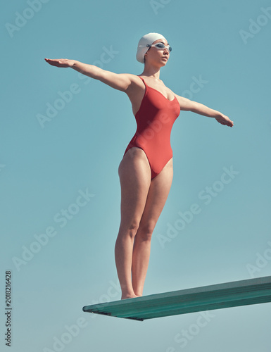 Fotografie Diving board, woman and stretching by blue sky for swimming, exercise or sport in swimwear by space