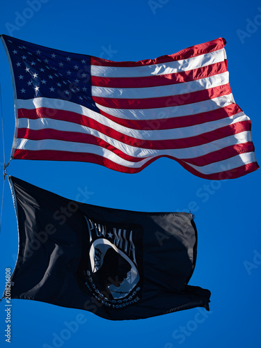 American flag waves beside POW banner. Patriotic American symbol honors veterans. United American heritage supports freedom. National American pride protects tradition.