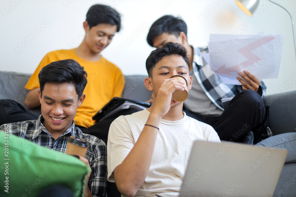 Fototapeta premium Group of Young Asian Men Smiling and Drinking Coffee While Working on Laptop