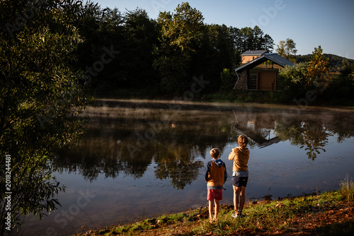 Boys fishing at sunrise lakeside with reflection