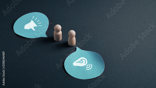Active listening concept with wooden figures and speech bubbles showing speaking and attentive ear communication