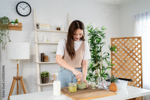 Asian young woman preparing matcha by stirring green tea powder in bowl.