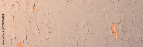 Peeling paint on the wall. Panorama of a concrete wall with old cracked flaking paint. Weathered rough painted surface with patterns of cracks and peeling. Wide panoramic texture for grunge background