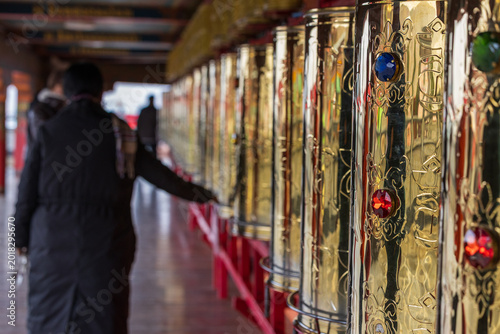 Tableau sur toile Pilgrims spinning prayer wheels inside the buddhist temple in Sehtar, Sichuan