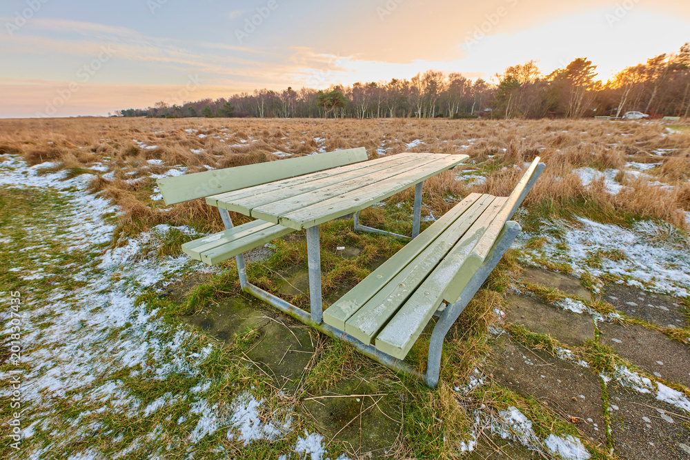 Obraz premium Landscape, sunset and winter with bench in park for sustainable environment and cold meadow. Natural ecology, snow and wilderness with conservation, countryside and field scenery of reservation