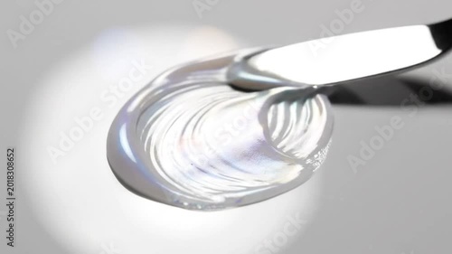 Iridescent liquid paint swirl being moved with a palette knife on a reflective surface in macro detail
