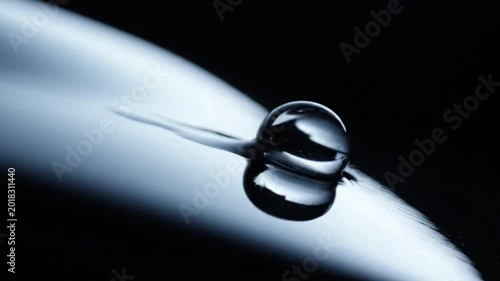 Extreme closeup of a single water drop forming two spheres on a dark, sleek surface, abstract macro photography