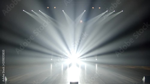 Empty performance stage with rustic wooden floorboards illuminated by moving white spotlights and smoke effects.