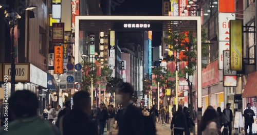 Ginza street in Tokyo city. Pedestrians walking through bustling commercial district street in night Japan. Surrounded by vibrant illuminated kanji signs. Dynamic urban scene. Luxury shopping travel