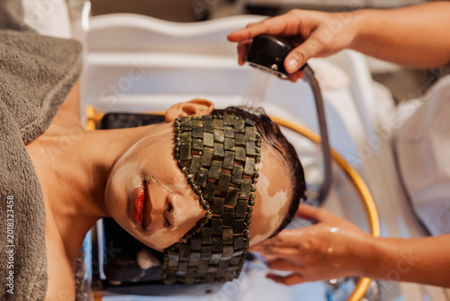Принти на полотні Spa therapist rinsing shampoo from a woman’s hair during a relaxing Japanese head spa treatment with jade eye mask therapy