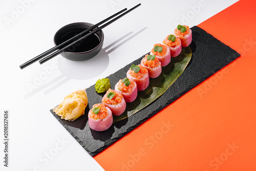 Pink sushi rolls on slate board with chopsticks